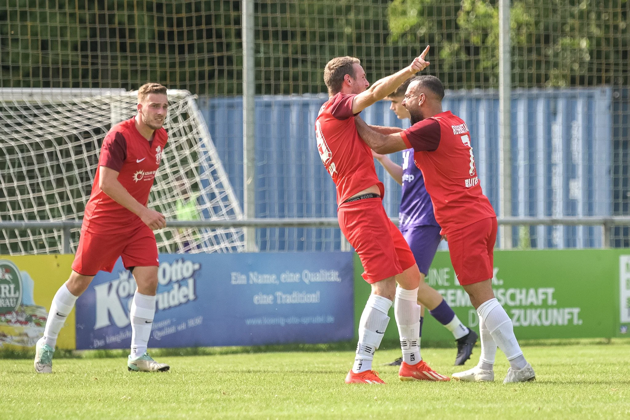 Fußballspieler in roten Trikots feiern ein Tor auf dem Spielfeld.