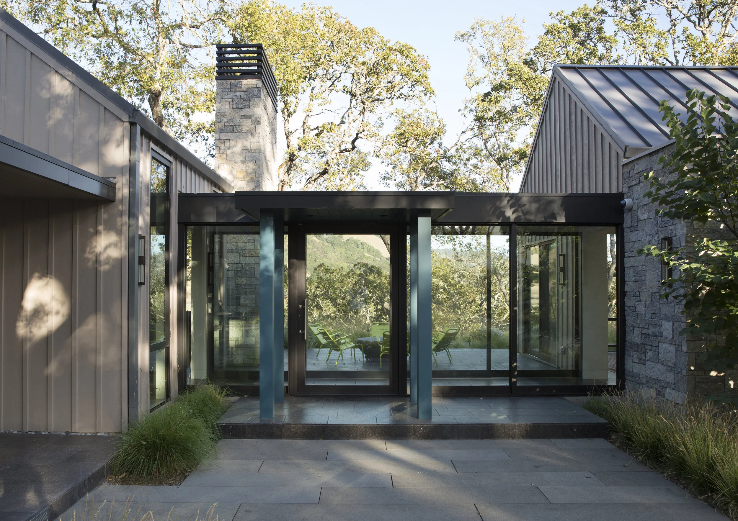 glass breezeway and stone veneer chimney connecting two wings of a modern farmhouse inspired residence in sonoma county at bennett valley with minimalist steel flat roofs and standing seam pitched roofs