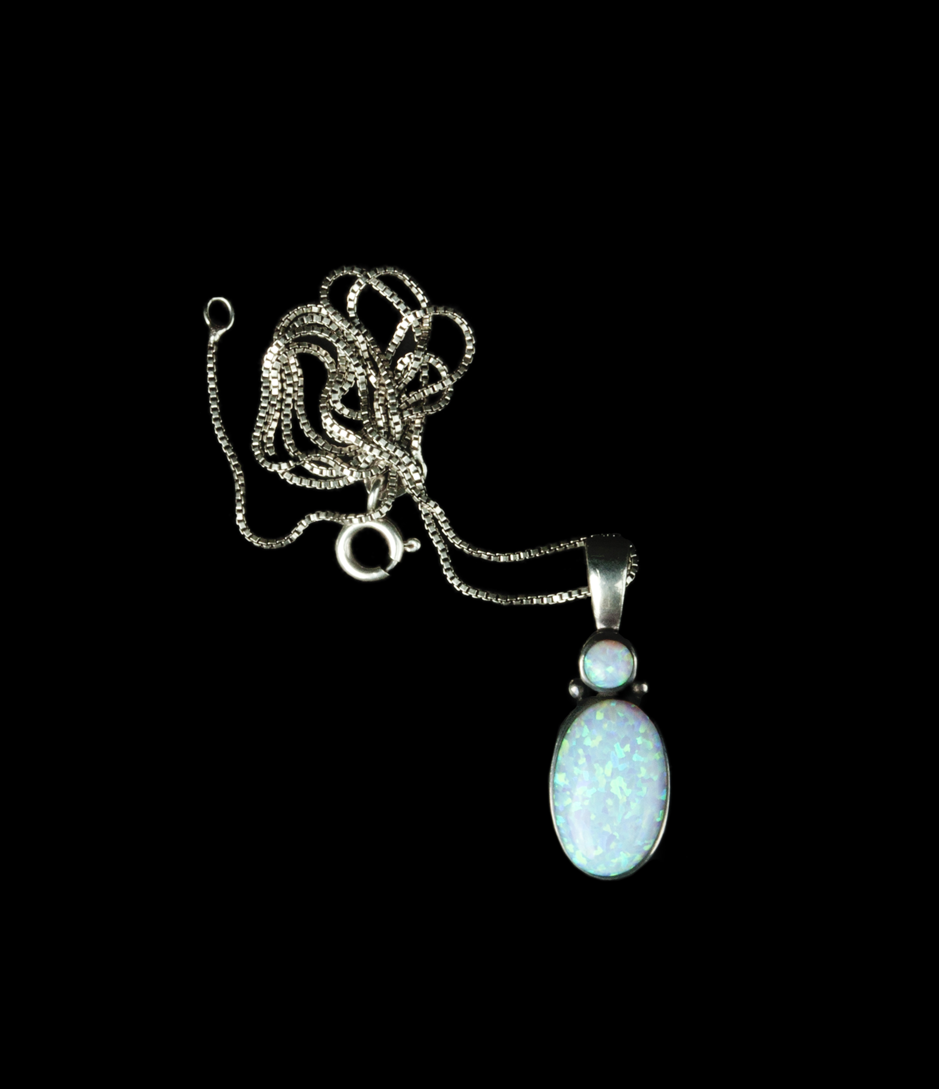  An oval moonstone pendant topped with a small round moonstone accent in a simple silver setting on a silver box chain which is coiled above it.   
