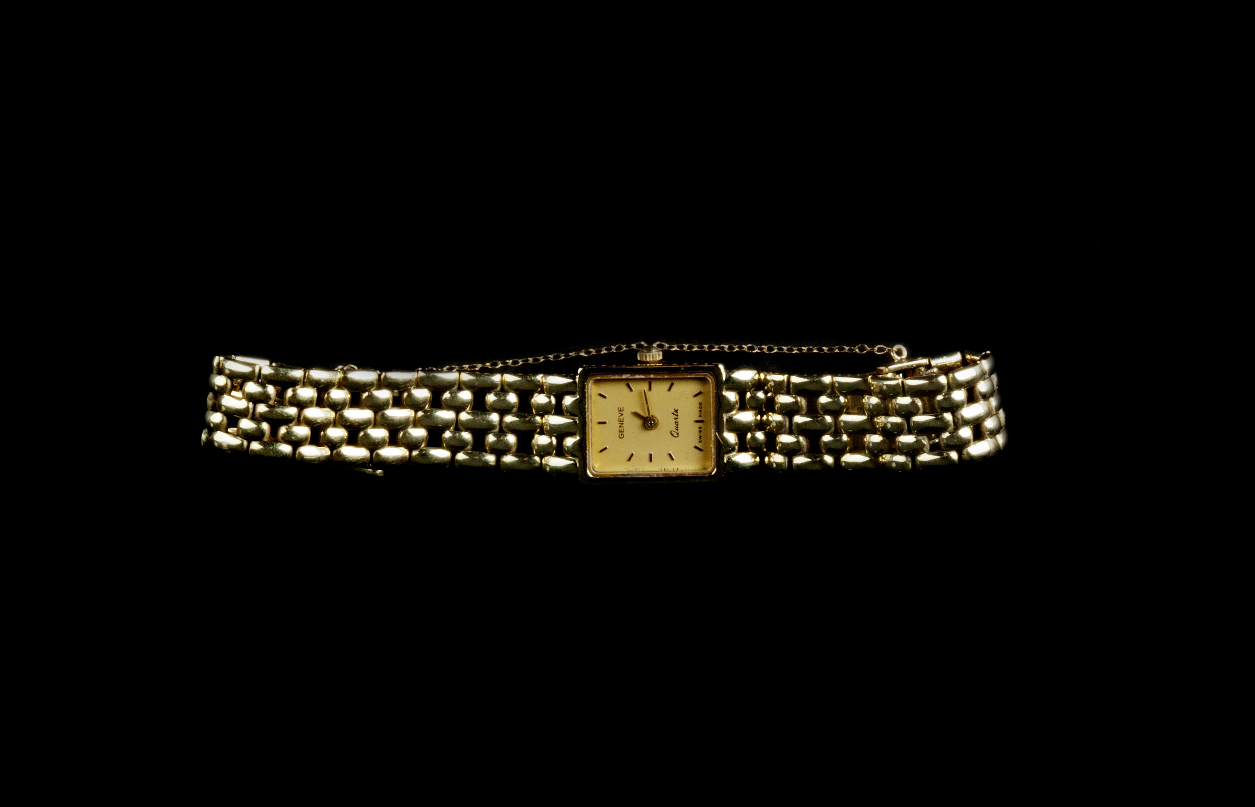  A square watch on a gold link band with a safety chain.  The watch is stretched out horizontally, showing the whole of its ivory face with roman numerals and gold pusher at the top. 