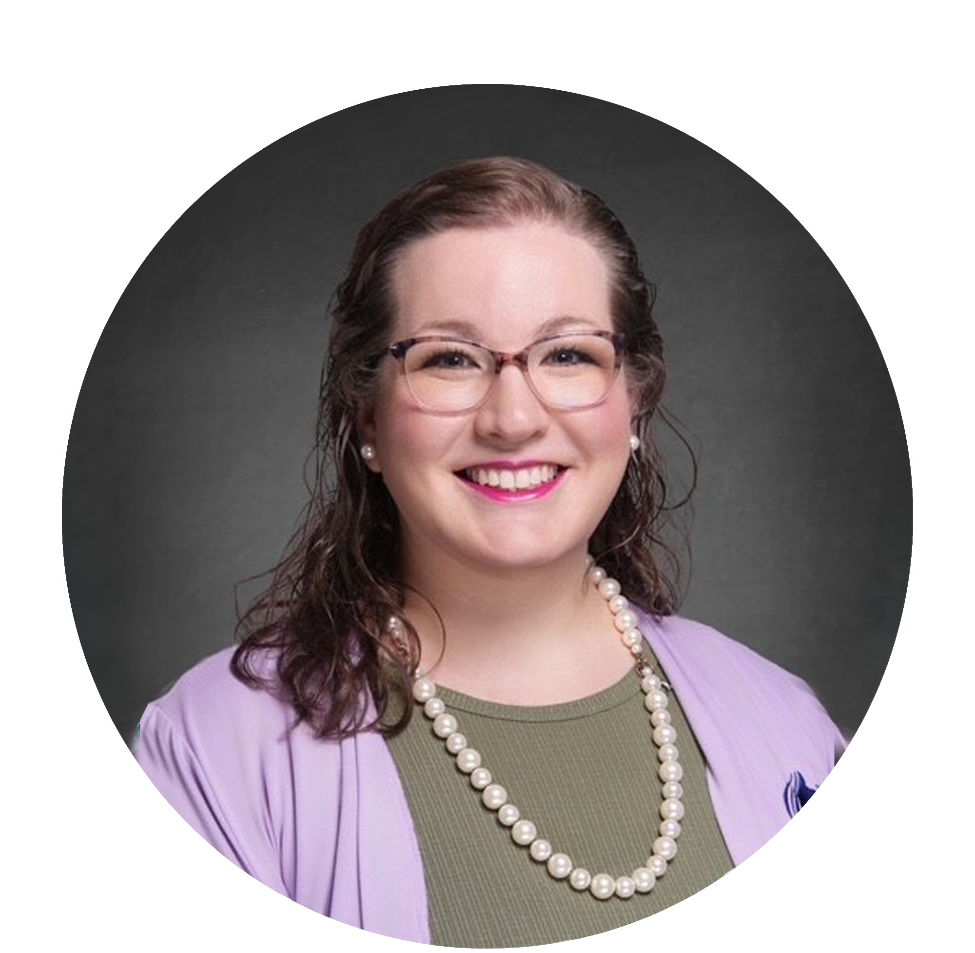Close-up of a smiling woman with glasses, pearl earrings, and a string of pearls, wearing a purple blazer and an olive-green top with a purple ribbon brooch.
