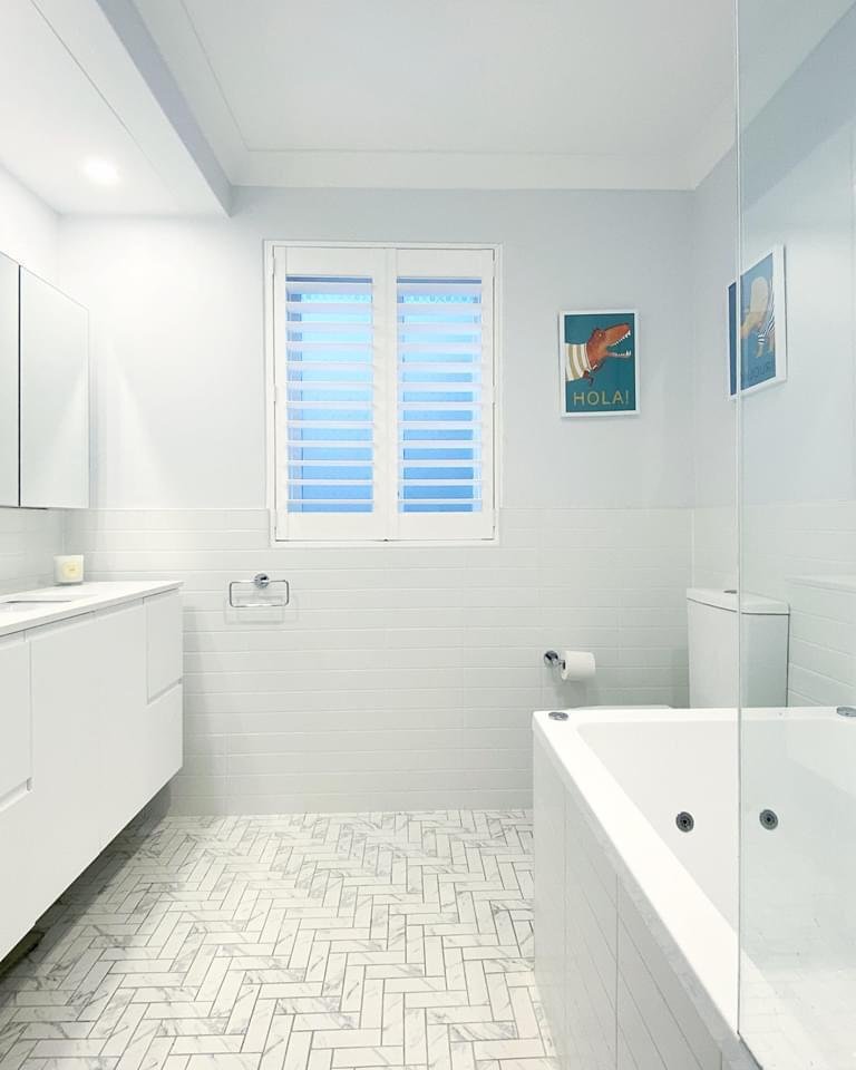  Sleek clean bathroom with herringbone tiled floor and wooden slat windows. 