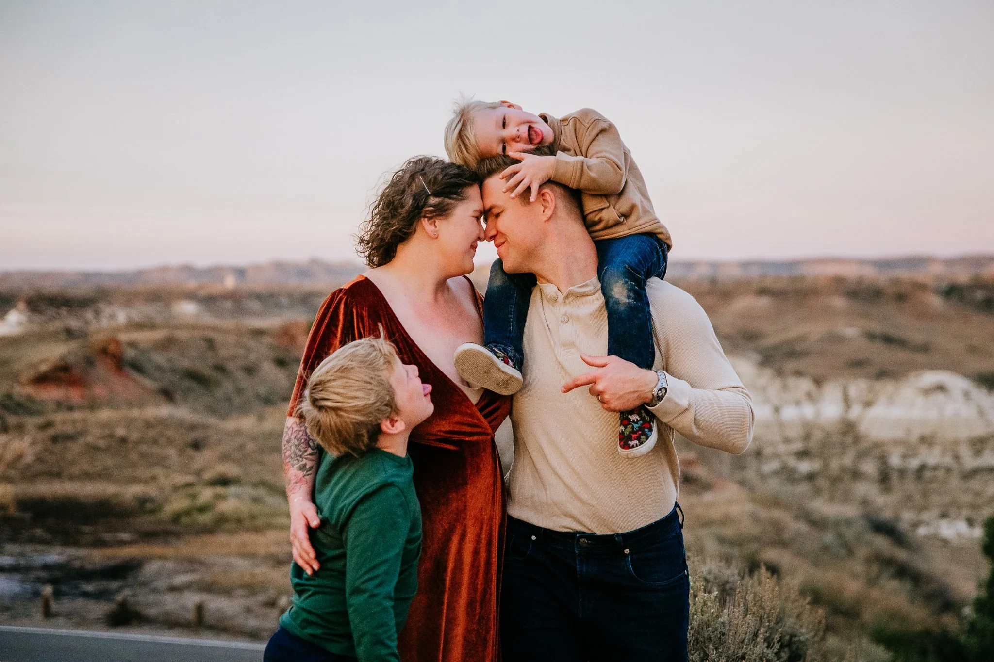 Family portrait of parents embracing forehead-to-forehead while their two sons climb on them, western North Dakota family photographer