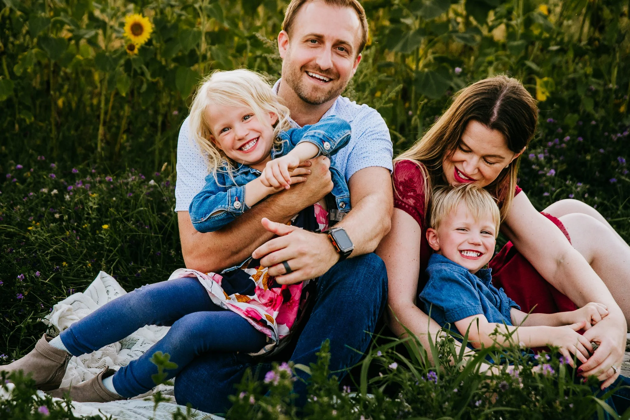 Family of four laughing together on a blanket in a sunflower field, family photographer in Dickinson, North Dakota