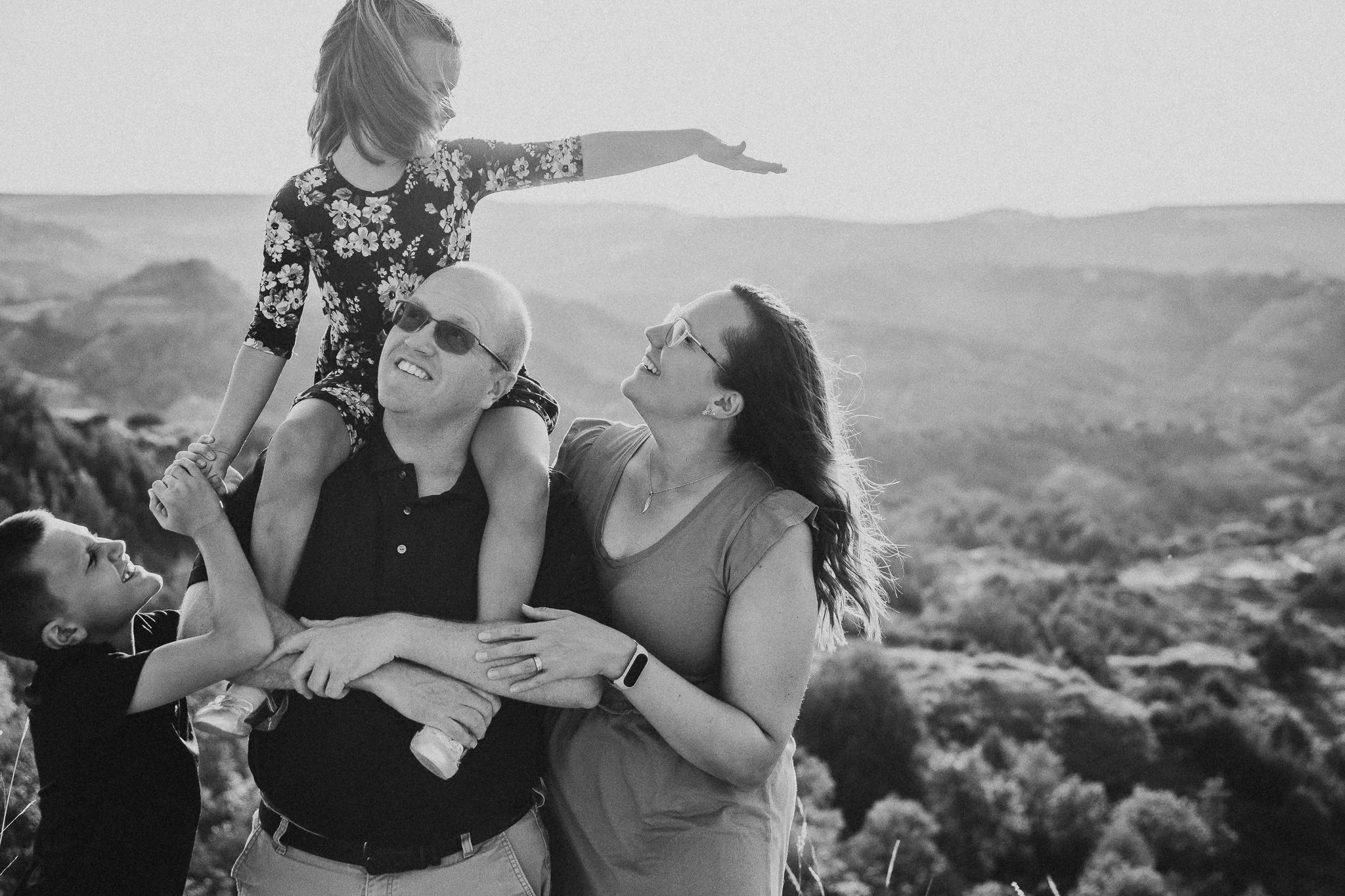 Black and white family portrait of parents laughing with their kids on an overlook in the North Dakota Badlands near Painted Canyon