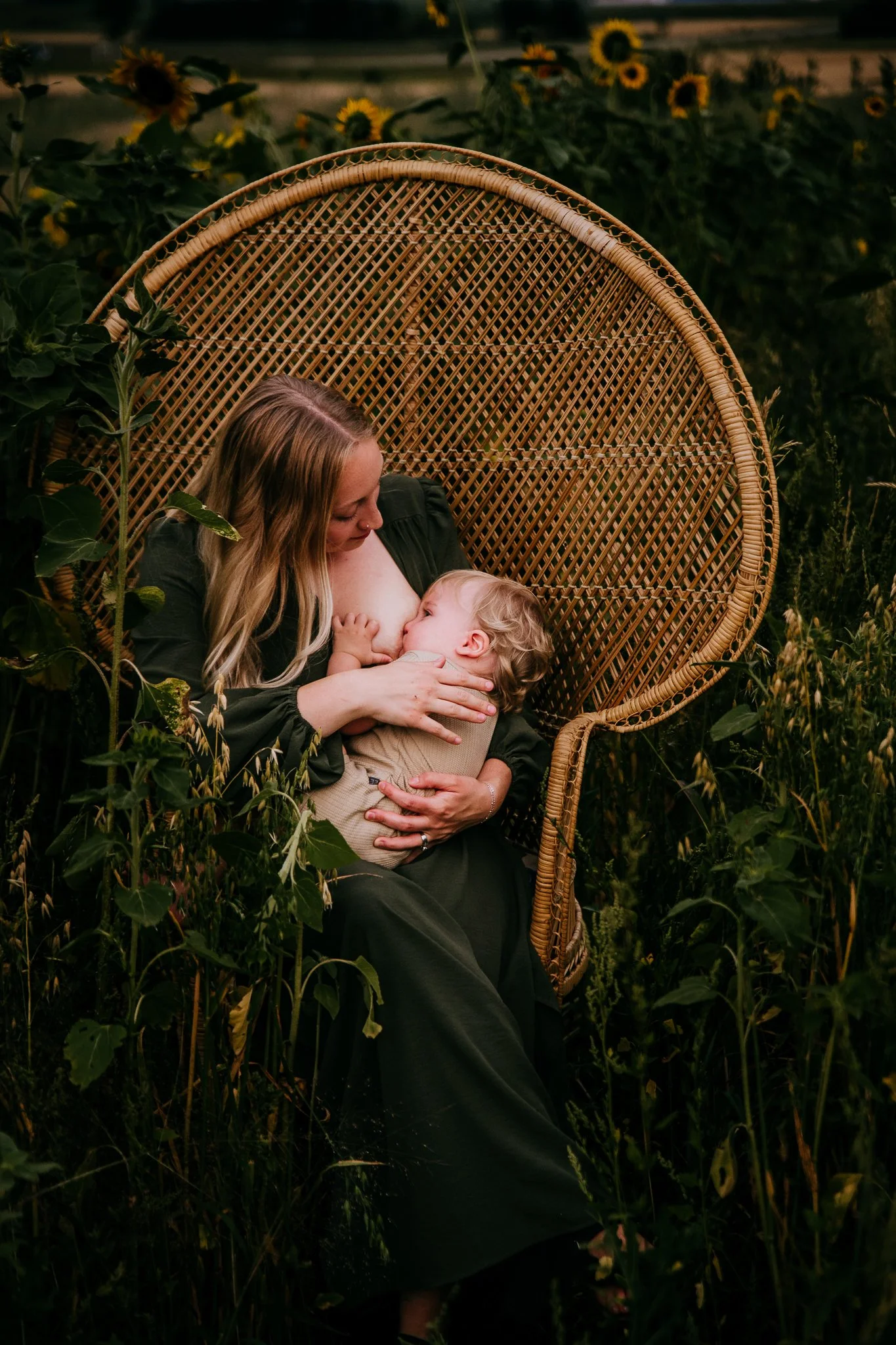 Mom in green dress breastfeeding toddler in peacock chair surrounded by wildflowers, North Dakota