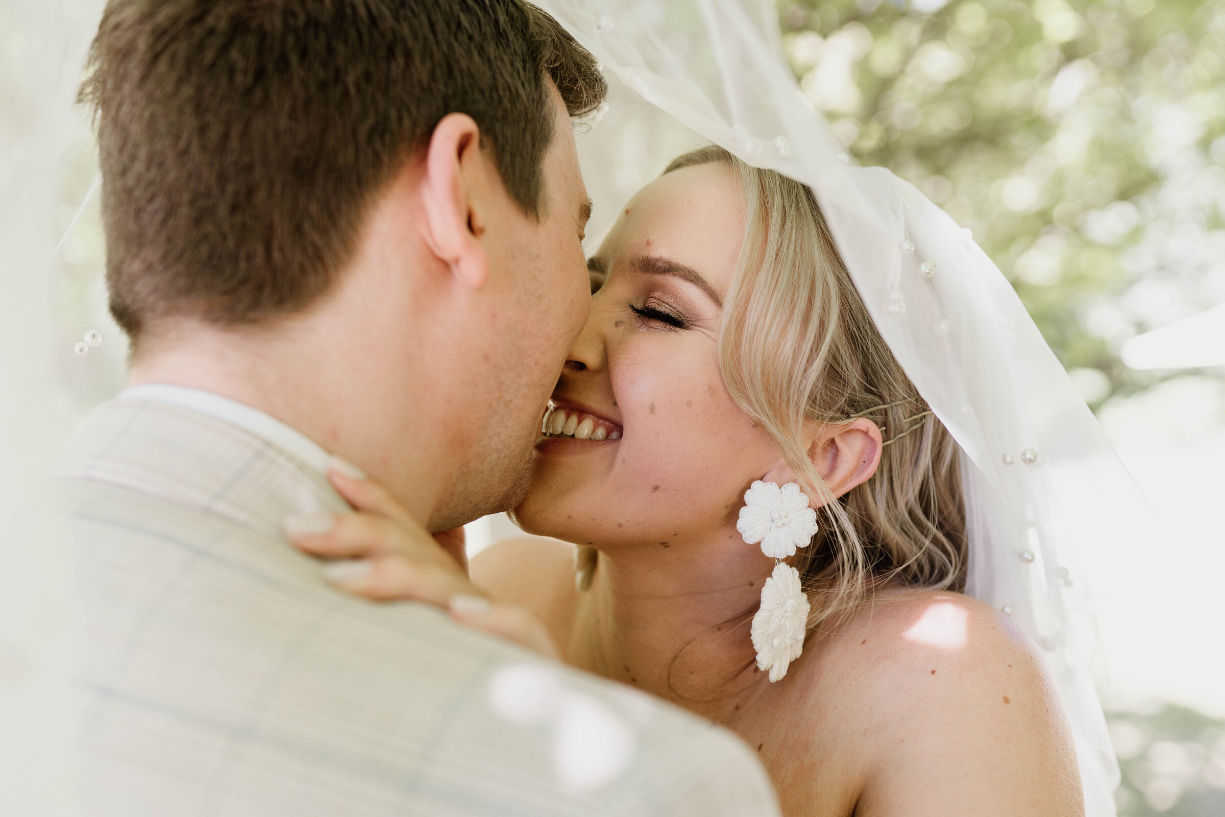 Bride and groom sharing kiss under pearl-covered veil