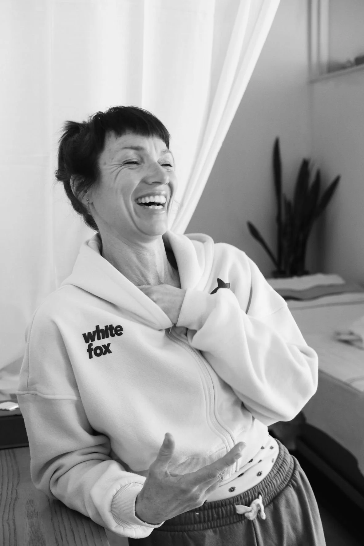 Kate laughs in a relaxed pose in-front of her massage studio