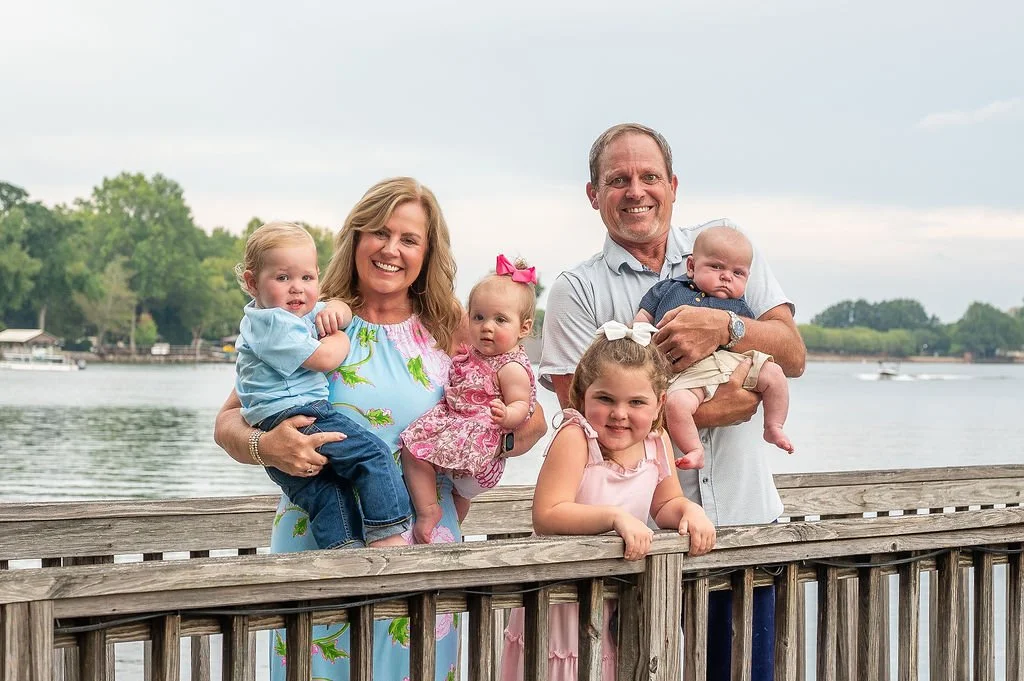grandparents hold their grandchildren while standing on pier at lake norman