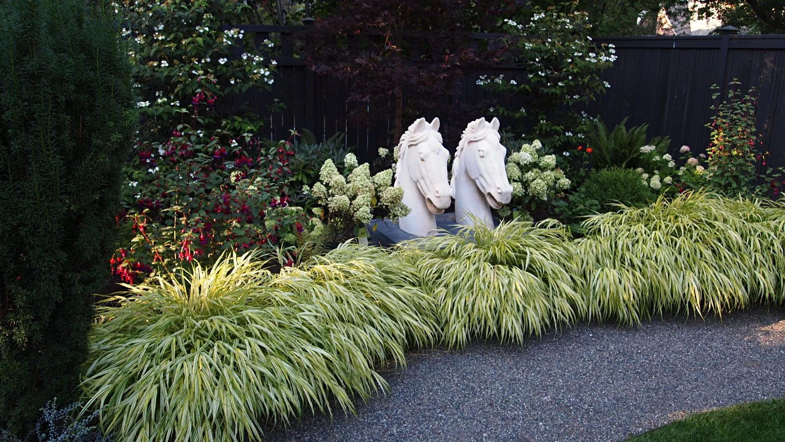20TH CENTURY MARBLE HORSE HEADS ON A CONCRETE BASE CREATE THE CENTRAL FOCAL OF THE GARDEN