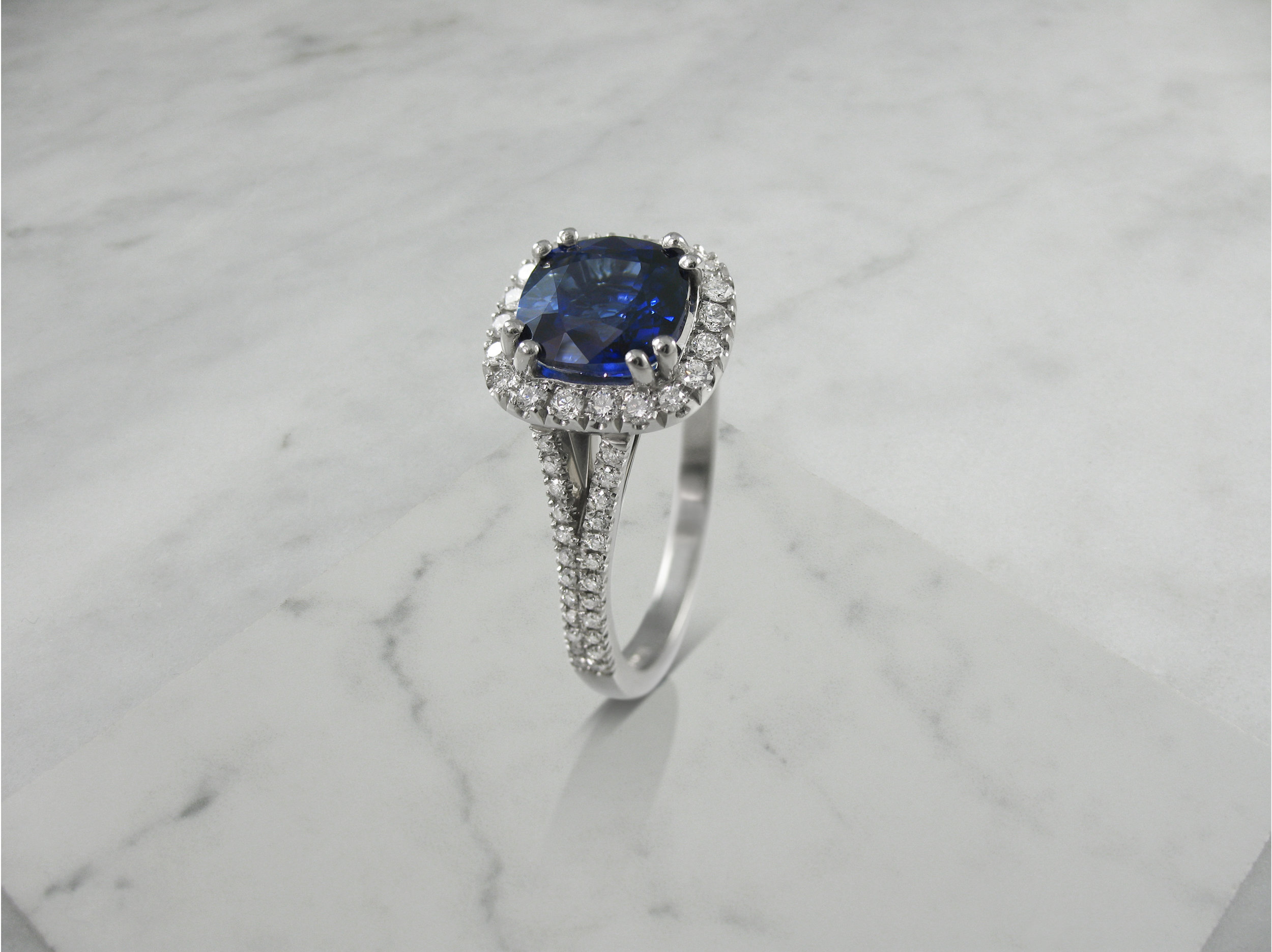 Cushion shaped sapphire and diamond halo engagement ring with split diamond band