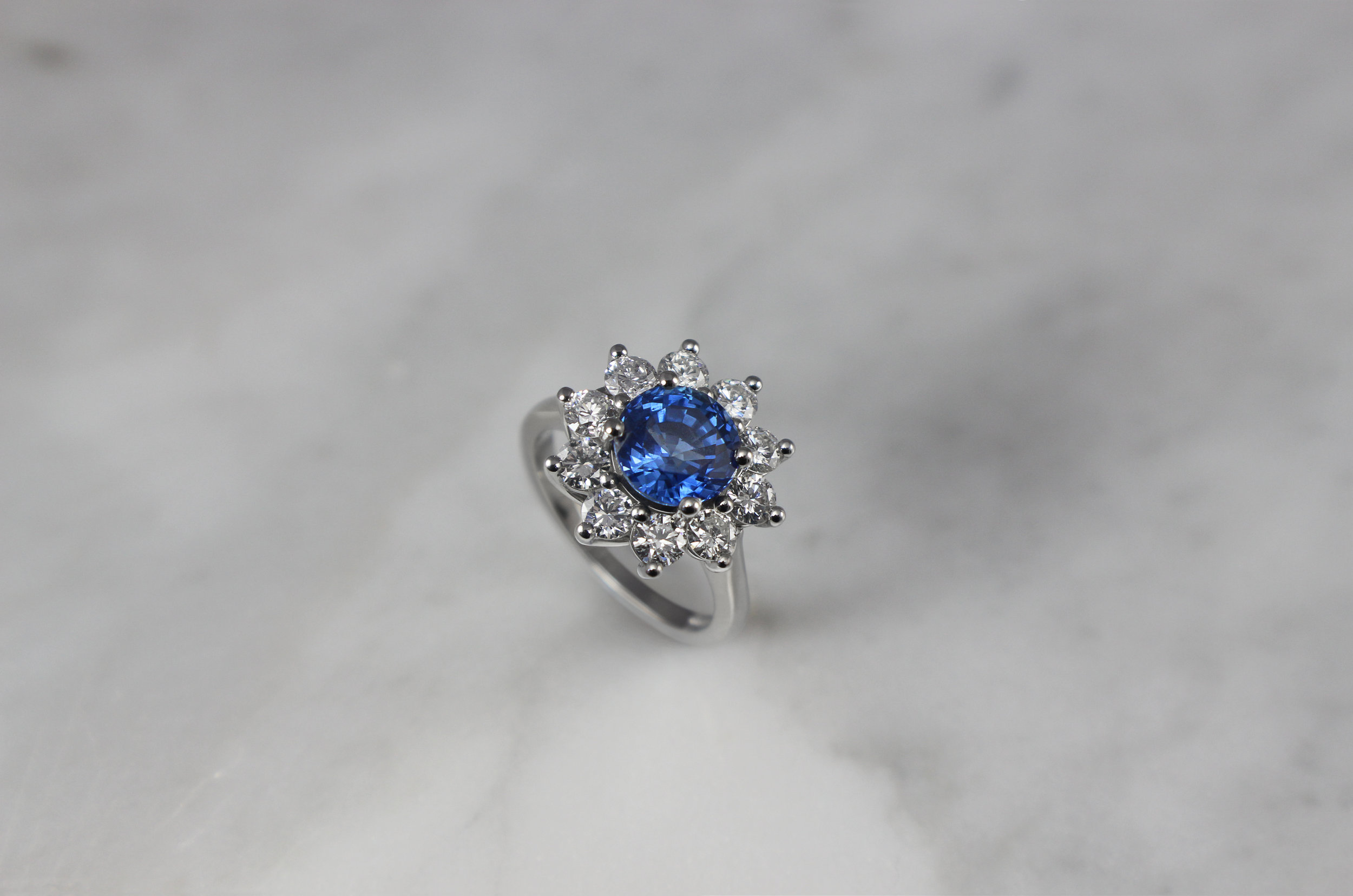 Round sapphire and diamond cluster engagement ring