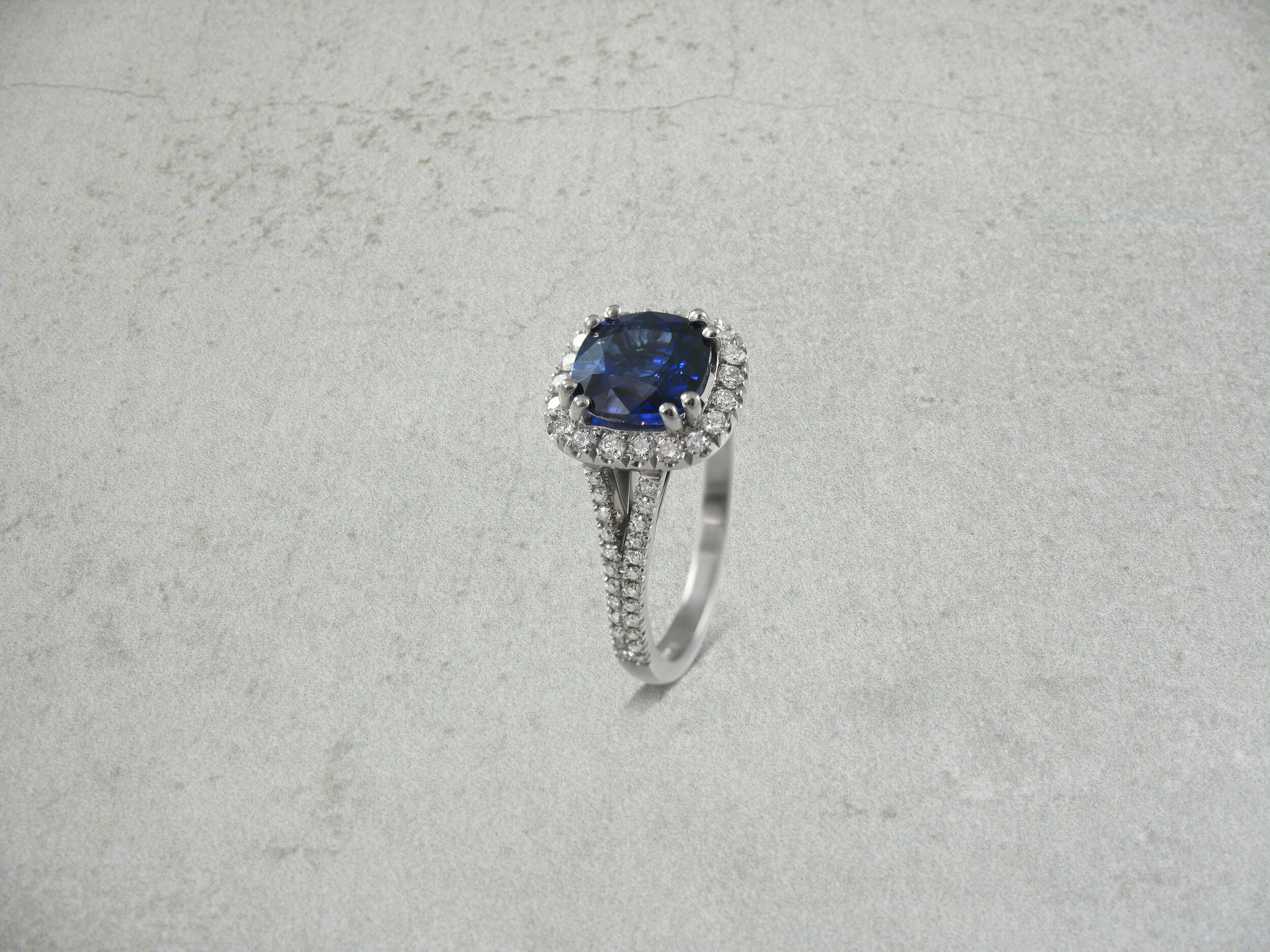 Cushion shaped sapphire halo ring with a diamond split shank