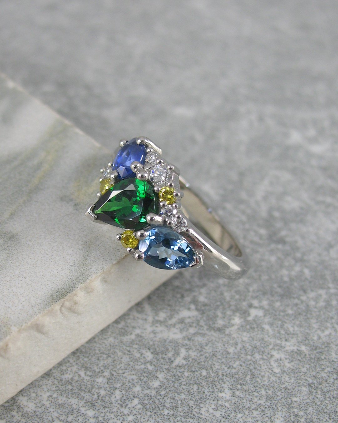 A colourful cluster ring featuring an oval sapphire, pear shaped tsavorite garnet, a pear shaped aquamarine and diamonds