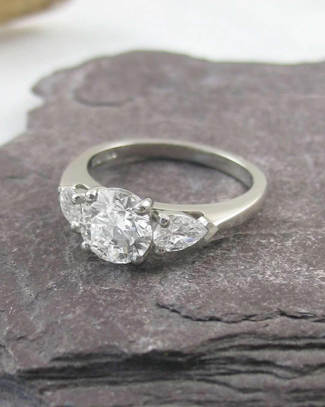 A dazzling round cut centre stone complemented by matching pear-shaped diamonds on the shoulders, creating a graceful and timeless three stone ring..jpg