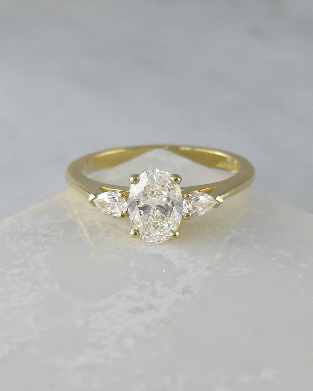 Oval diamond engagement ring with pear-shaped side diamonds in yellow gold