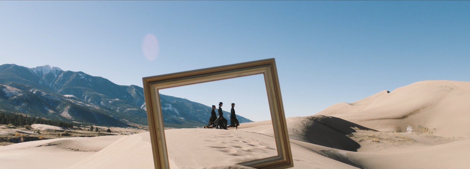 large wooden photo frame at the middle of the desert with three people walking