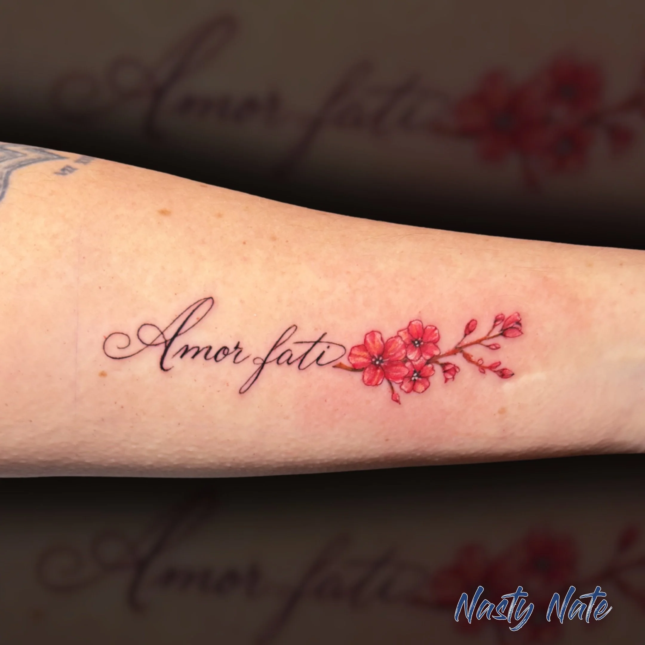 Amor fati - love of fate. ❤️ @tattoos_by_nastynate absolutely crushed the elegant flow on this script piece. Pulling off fine line lettering this crisp takes a steady hand, and the way the text seamlessly transitions into those vibrant cherry blossom