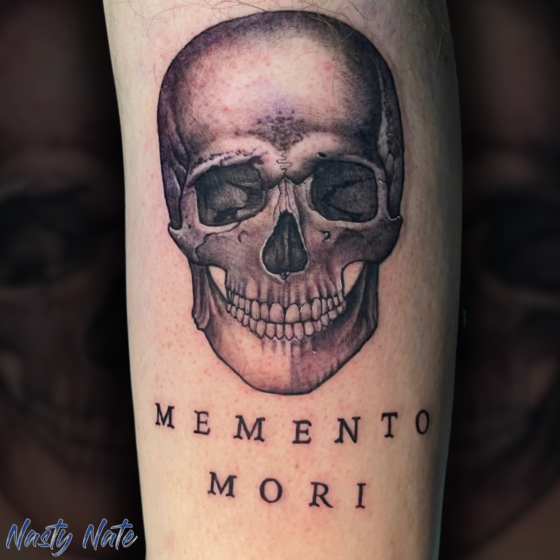 Memento Mori. 💀 @tattoos_by_nastynate killed this heavy-hitting black and grey skull and the precision on that lettering is spot on. If you appreciate clean illustrative shading and timeless dark concepts, Nate is definitely your artist. 

What clas