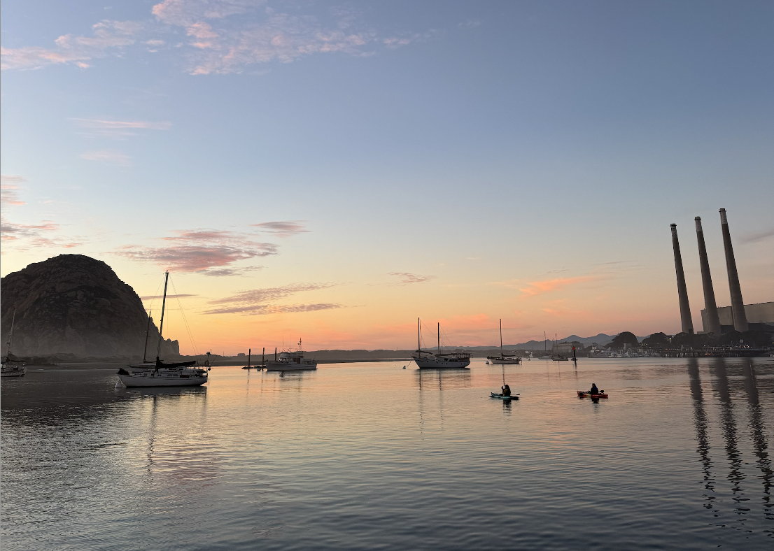 Morro Rock and the smoke stacks at sunset with boats and kayaks in the bay