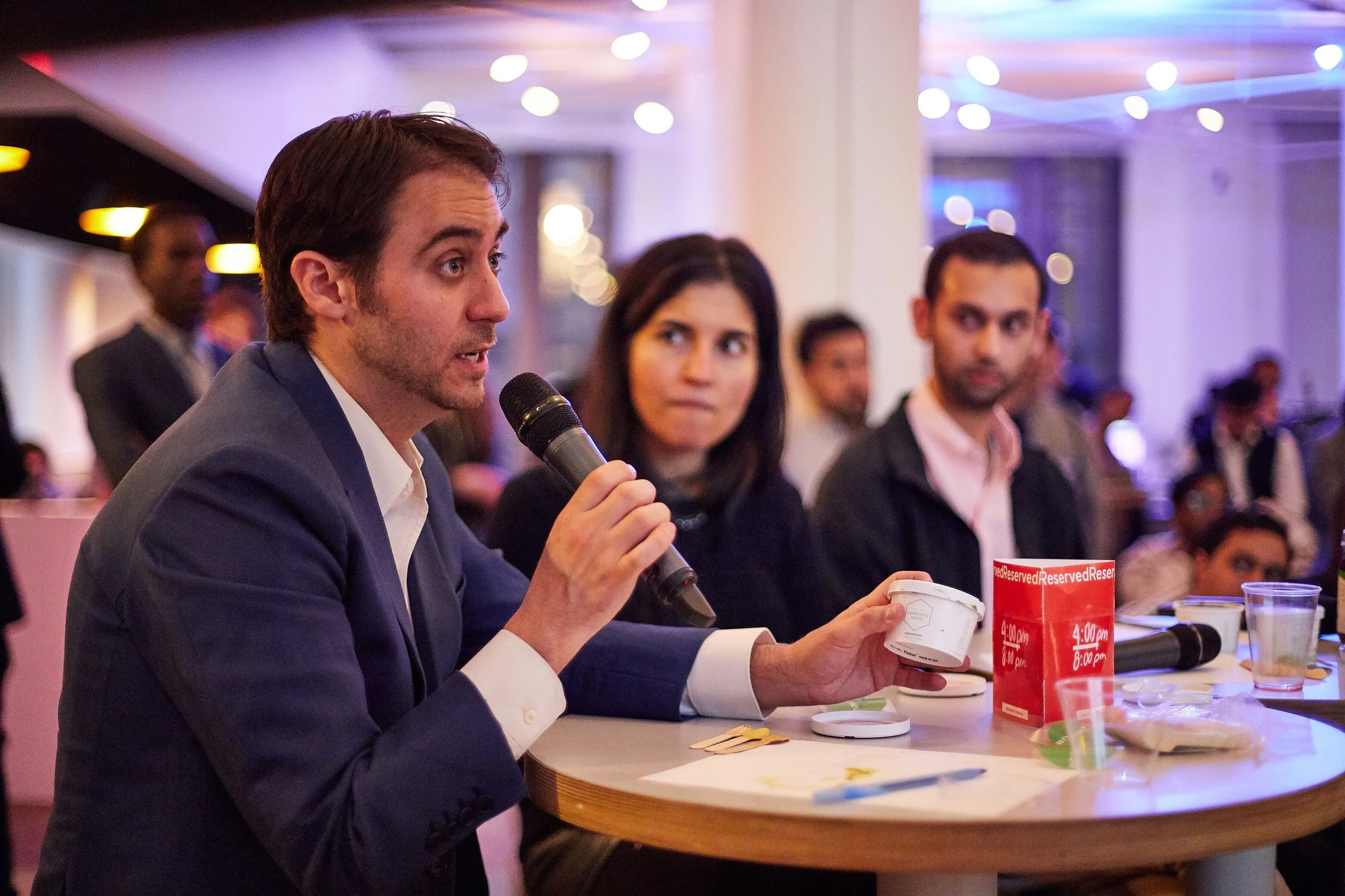 man-in-suit-speaking-at-event-table.jpeg