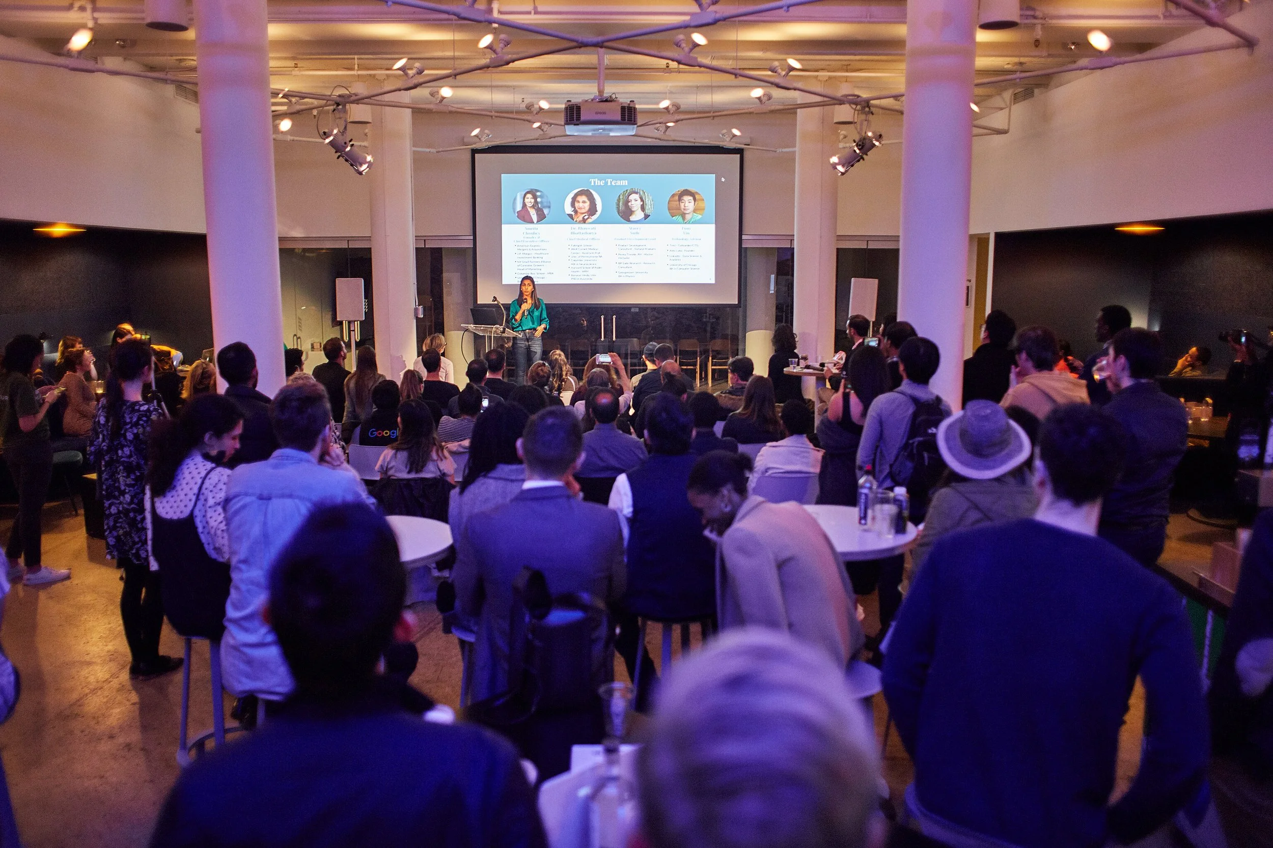 speaker-presenting-to-crowd-blue-lit-room.jpeg
