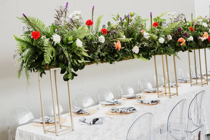 A closer look at the head table’s colorful combination of peach & white roses, Liatris, and deep purple & red carnations thoughtfully placed among an overflowing bouquet of greenery is reminiscent of a lush botanical garden.