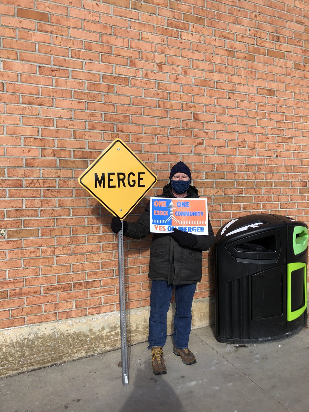 Mike Sullivan sports a “Merge” sign, indicating support for the proposed merger between Essex Jct. and Essex Village on the ballot Tuesday. (Jen Lannom/Community News Service)