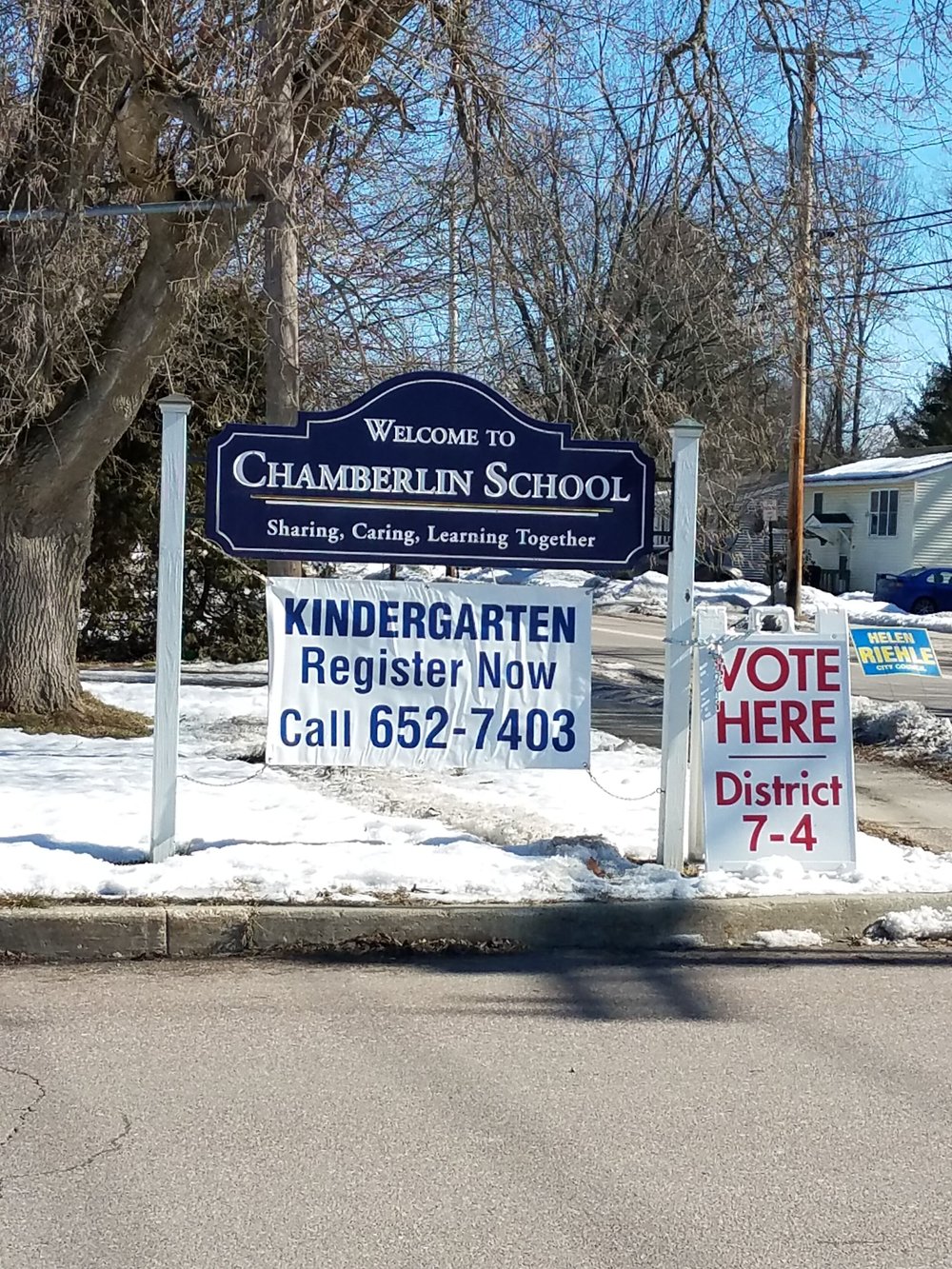 The sign leading into the Chamberlin School polling location, surrounded by yard signs stuck into the icy snow. (Claire MacQueen/Community News Service)