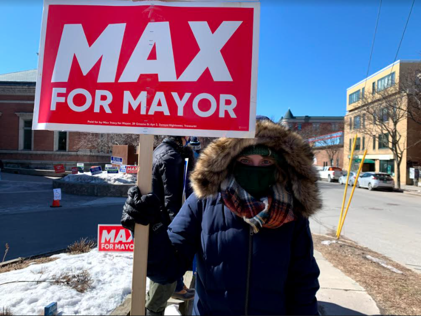Jane Stromberg holds a “Max for Mayor” sign outside of the Fletcher Free Library. (Mae Nagusky/Community News Service)]