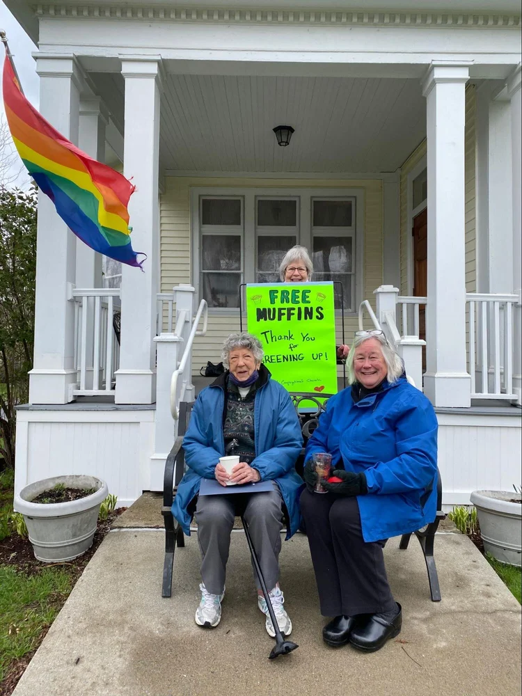 Carol Adams (left), Ingrid Cichoski (right), and JoEllen Swaine (center) distribute free muffins and coffee in compostable bags and cups to Green Up Day participants outside of the Richmond Congregational Church on Saturday May 1, 2021. ( Emily Shedd/Community News Service)