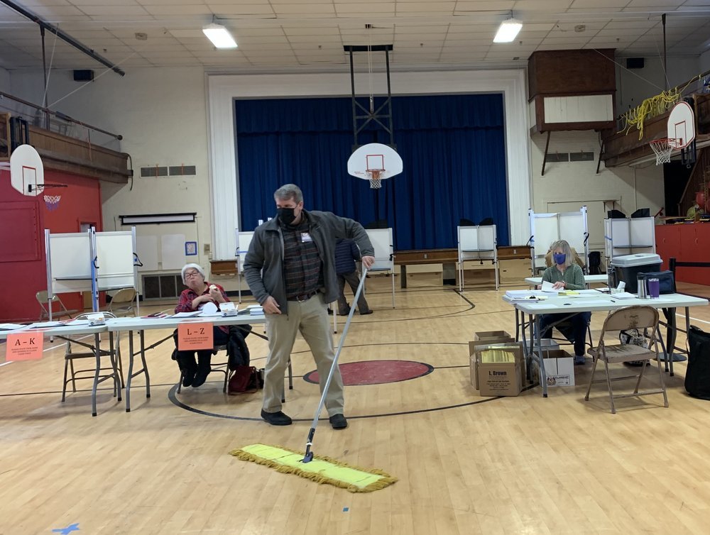   During a calm moment at the polls inside the Brookside gym, Waterbury elections official Chris McKay sweeps away grit and snowmelt tracked in on voters' boots. Looking on are elections official Pauline Nolte (left) and Assistant Town Clerk Beth Jon