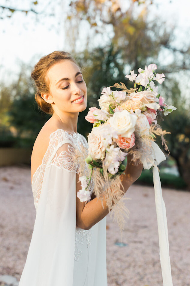 Mariée blonde souriant et regardant son bouquet de fleurs pendant son mariage.