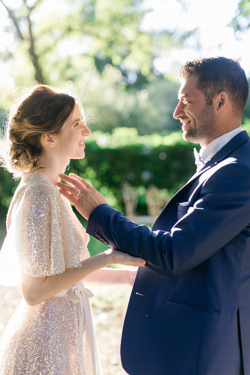 Le couple se retrouvant pendant le first look, se souriant l'un l'autre, et le marié pose sa main sur la joue de sa femme.