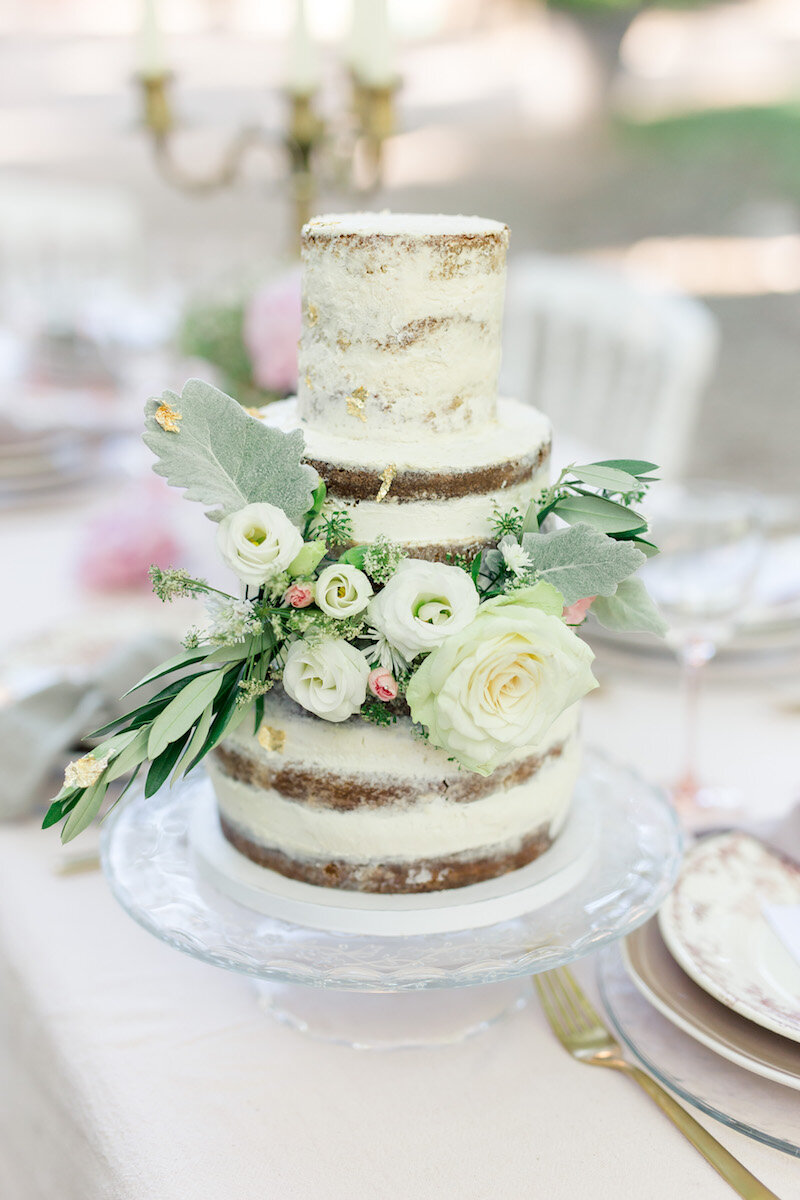 Zoom sur le wedding cake posé sur la table. Cela s'appelle un naked cake parce qu'on apperçoit la génoise sous la crème, et le gâteau est orné de fleurs.