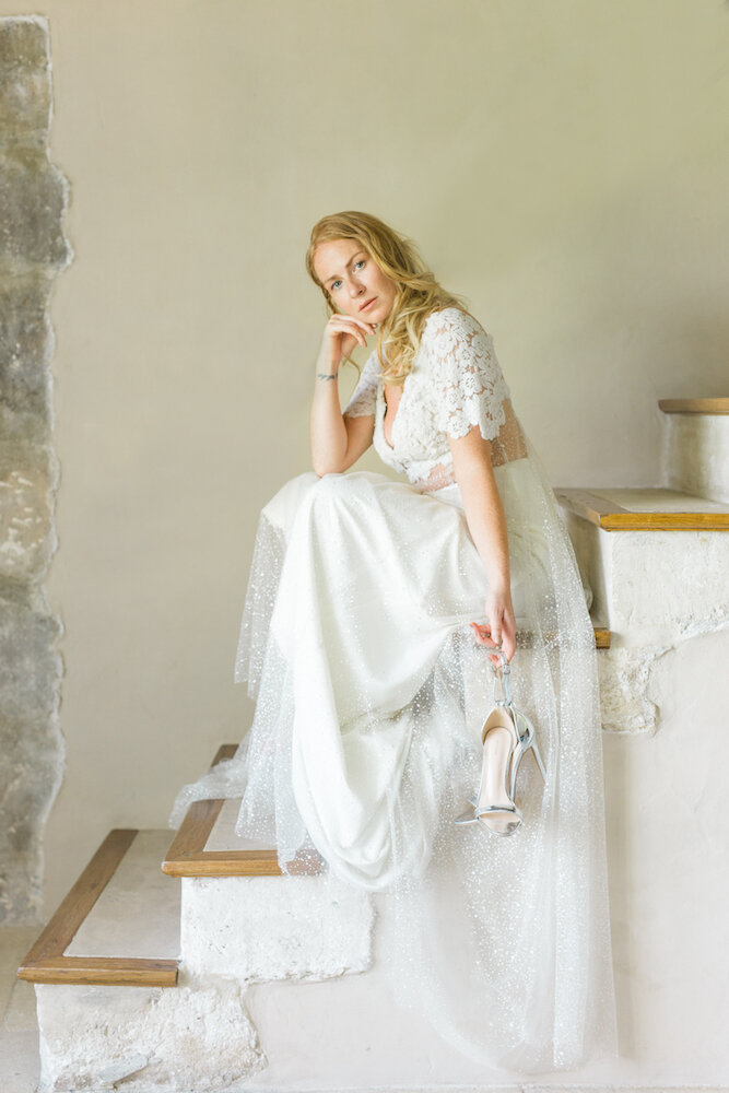 la mariée dans sa jolie robe qui pose assise sur les escaliers intérieurs du mas de la rose en Provence et qui prend une pose mode