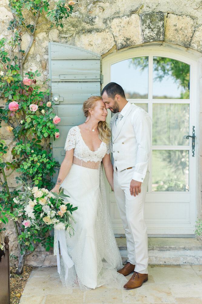 Photo de couple lors d'un shooting mariage. Les mariés se tiennent debout, front contre front, et la mariée tient son bouquet de fleurs.