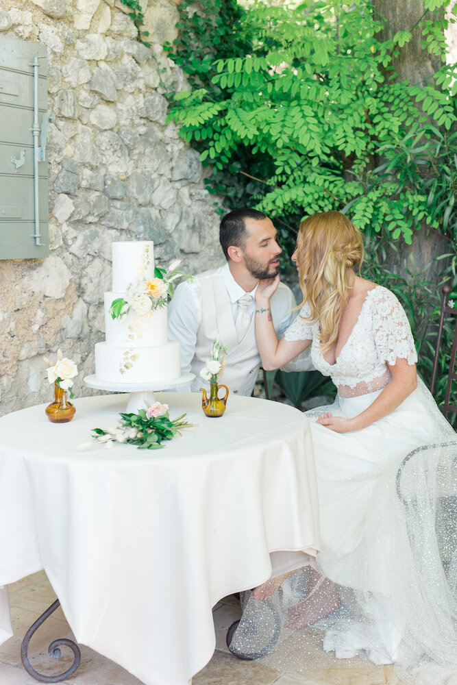 Le couple de mariés assis devant la table contenant le wedding cake, ils se regardent et vont s'embrasser.