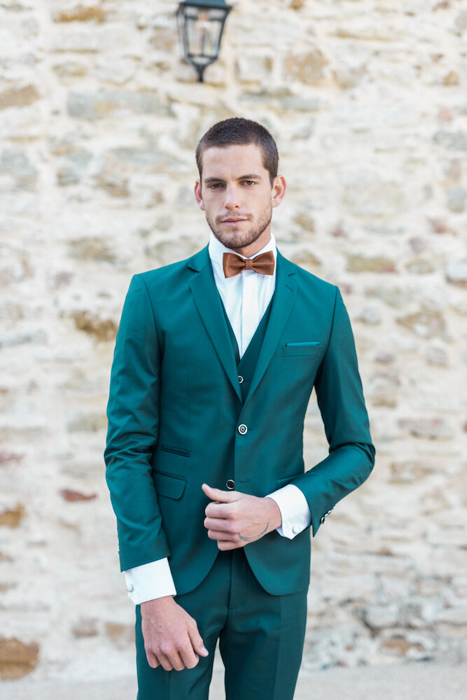 The groom posing in front of the camera, with a beautiful green tree suit.