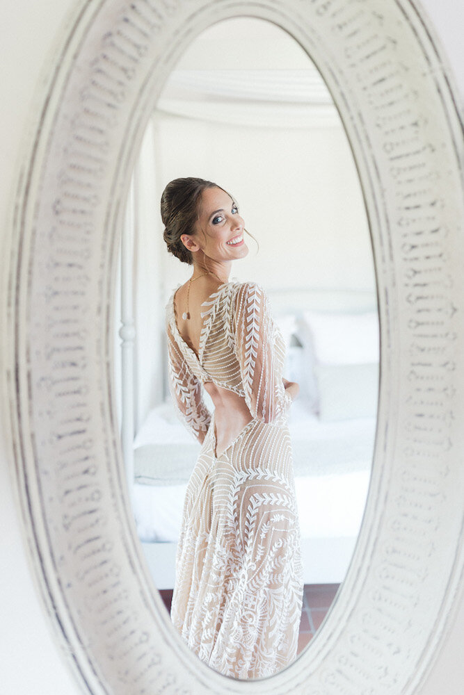 During the preparations, the bride is discovering her reflection in the mirror with her beautiful beige and white dress.