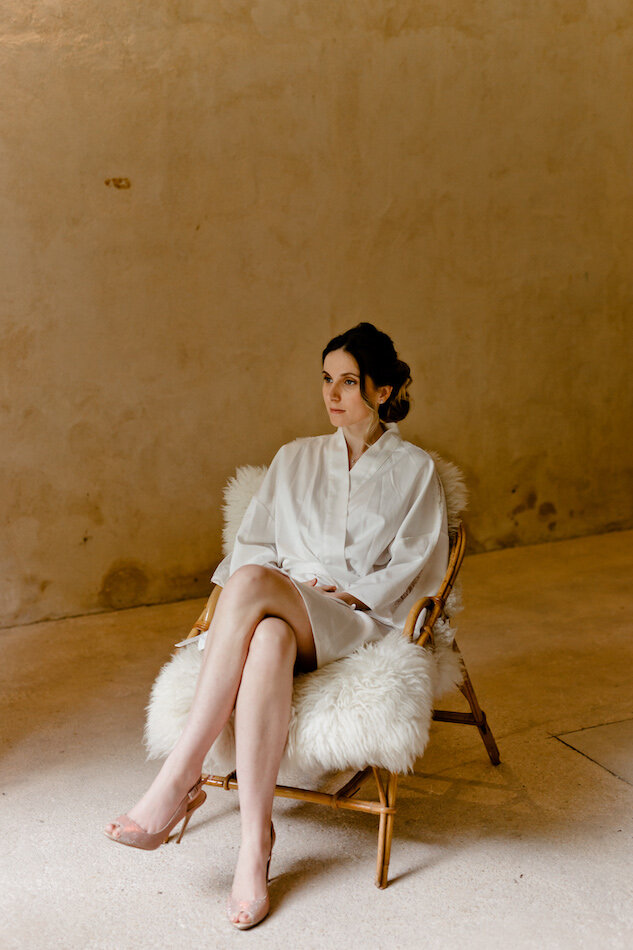 La mariée pendant les préparatifs dans son peignoir blanc en soie, assise dans un fauteuil.