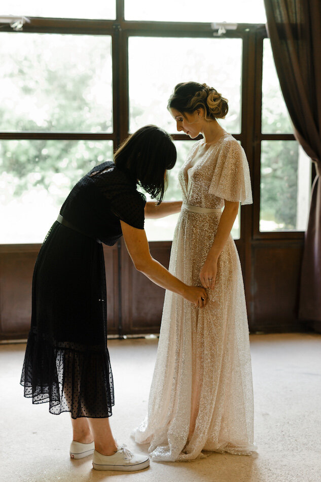 Vue sur la créatrice qui arrange la robe de mariée sur la modèle.