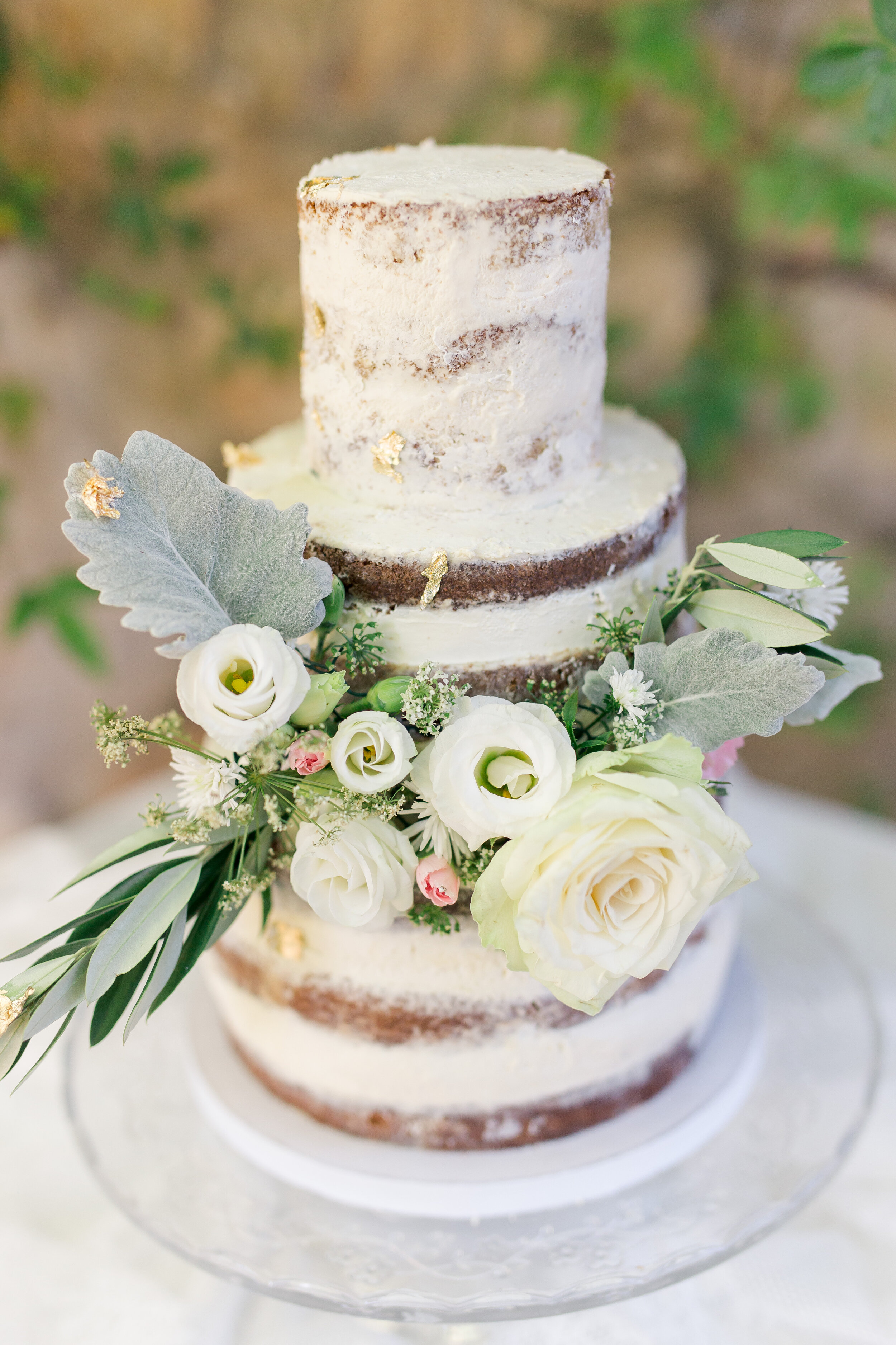 Gros plan sur le wedding cake avec ses fleurs blanches et roses claires, et des feuilles d'or.