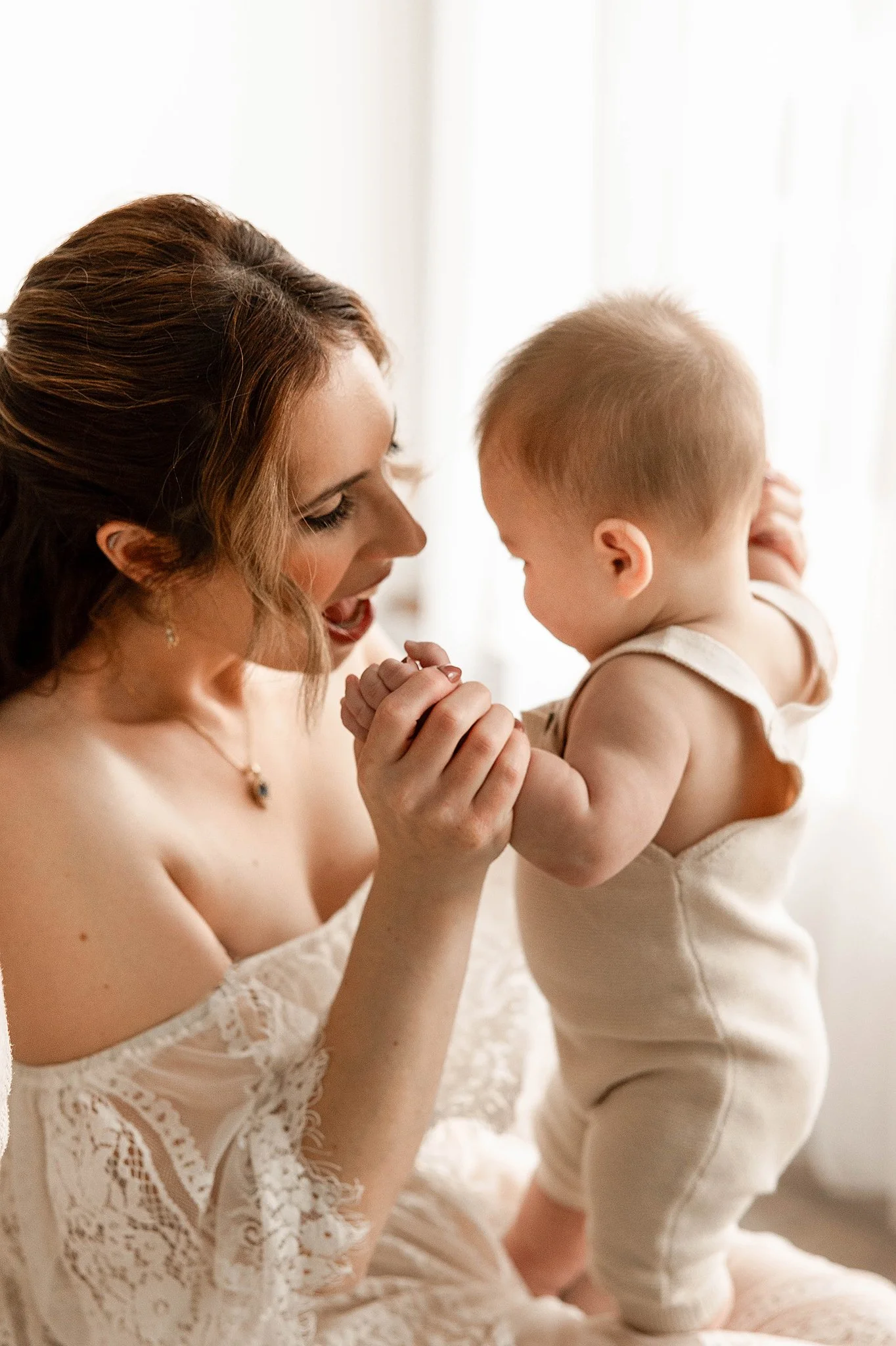 family photo of a mom and baby holding hands and smiling sweetly at each other in a natural light photography studio