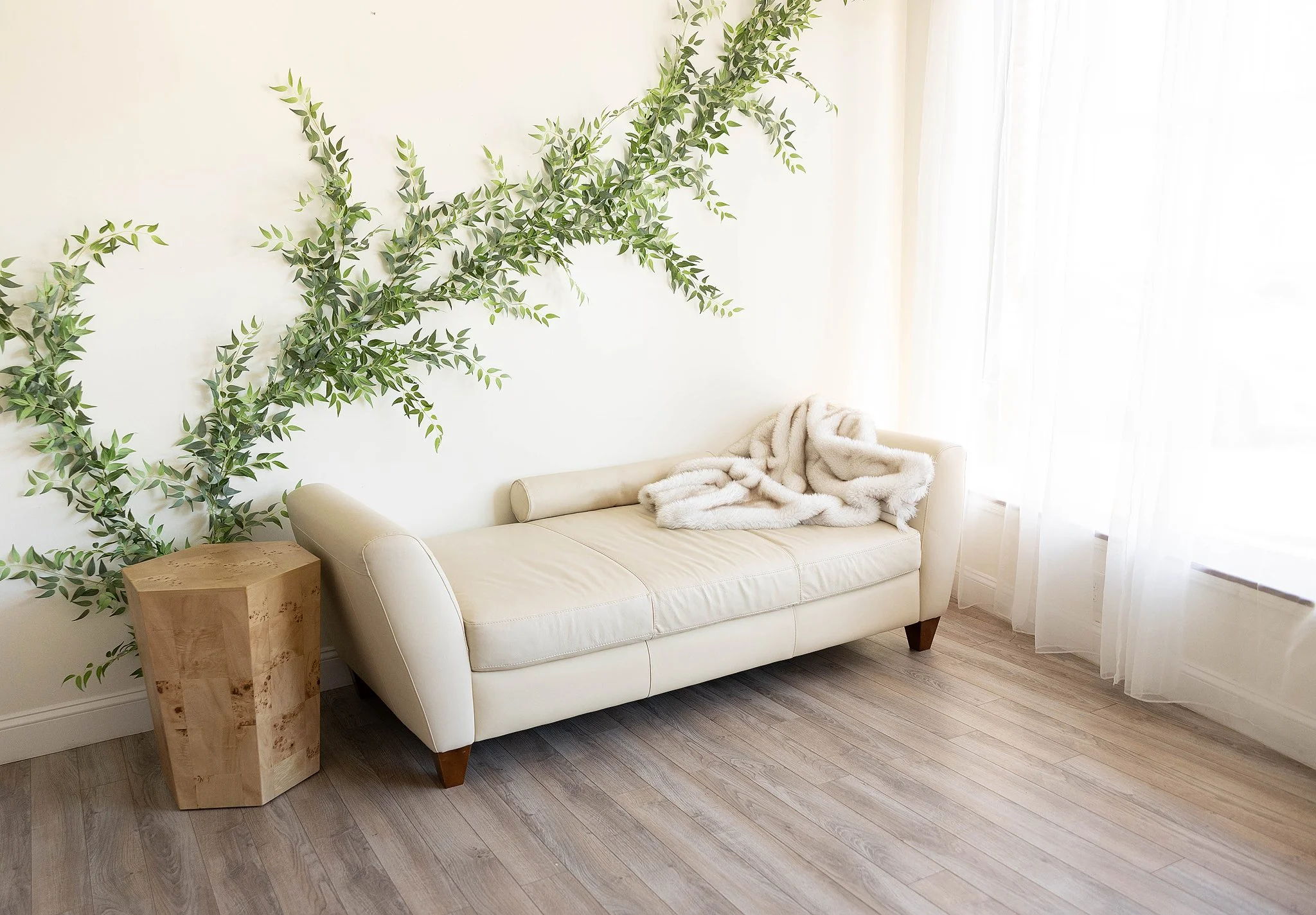natural light studio with an artistic greenry wall and ivory couch with ivory fur draped on it