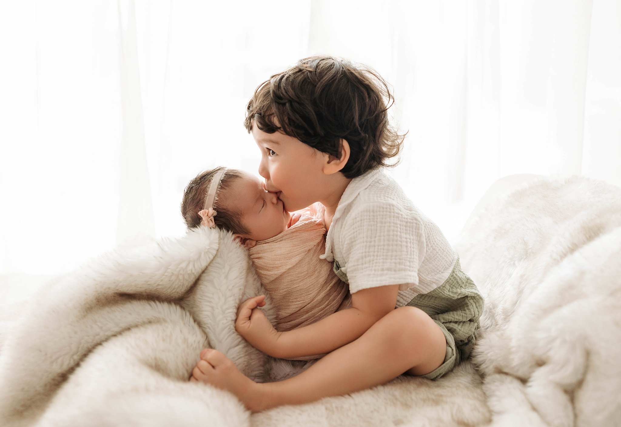 sibling photo of big brother holding his new baby sister and kissing her nose with pretty backlighting at Chelsie Maurer Photography studio