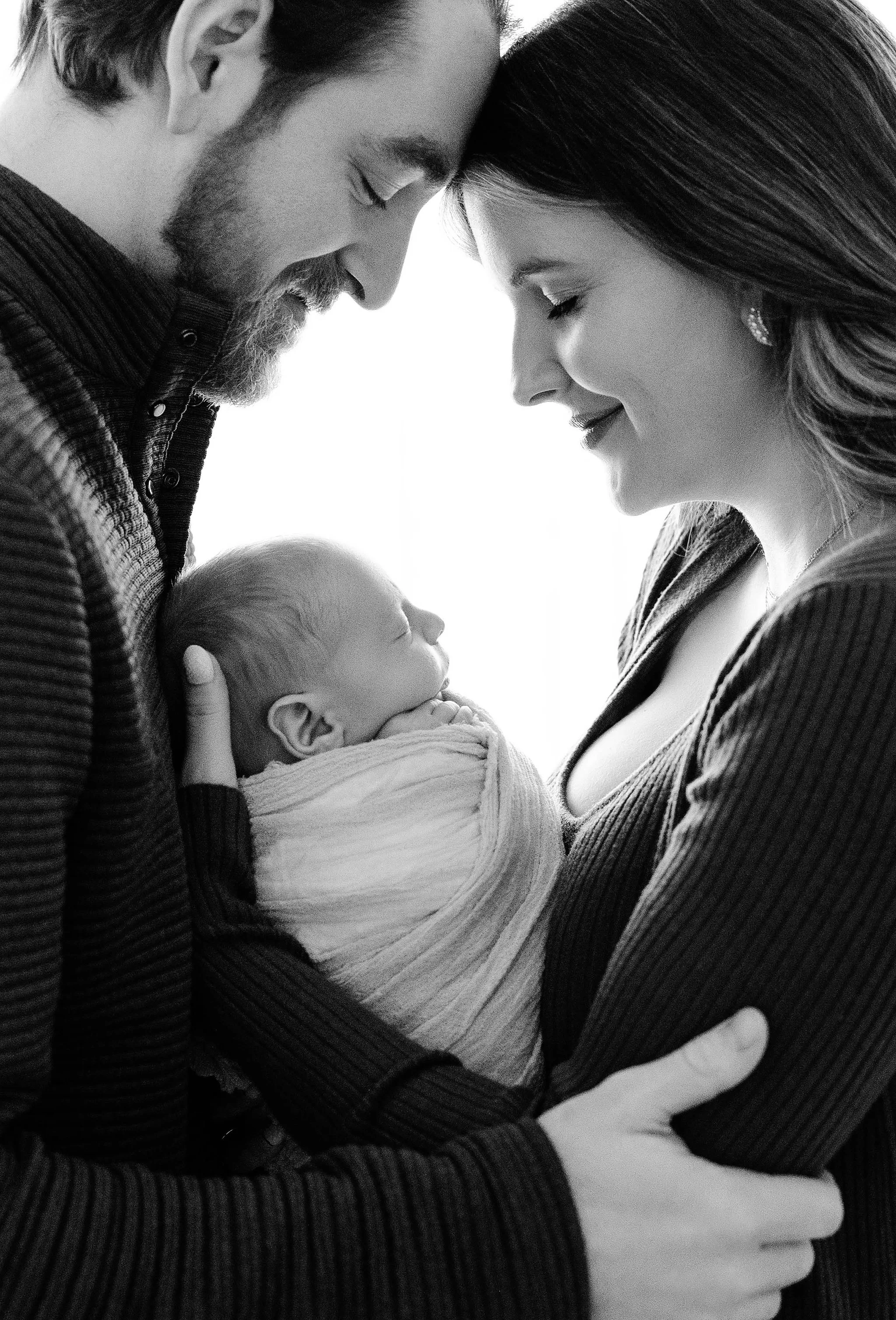 mom and dad standing towards each other with newborn baby boy in between them