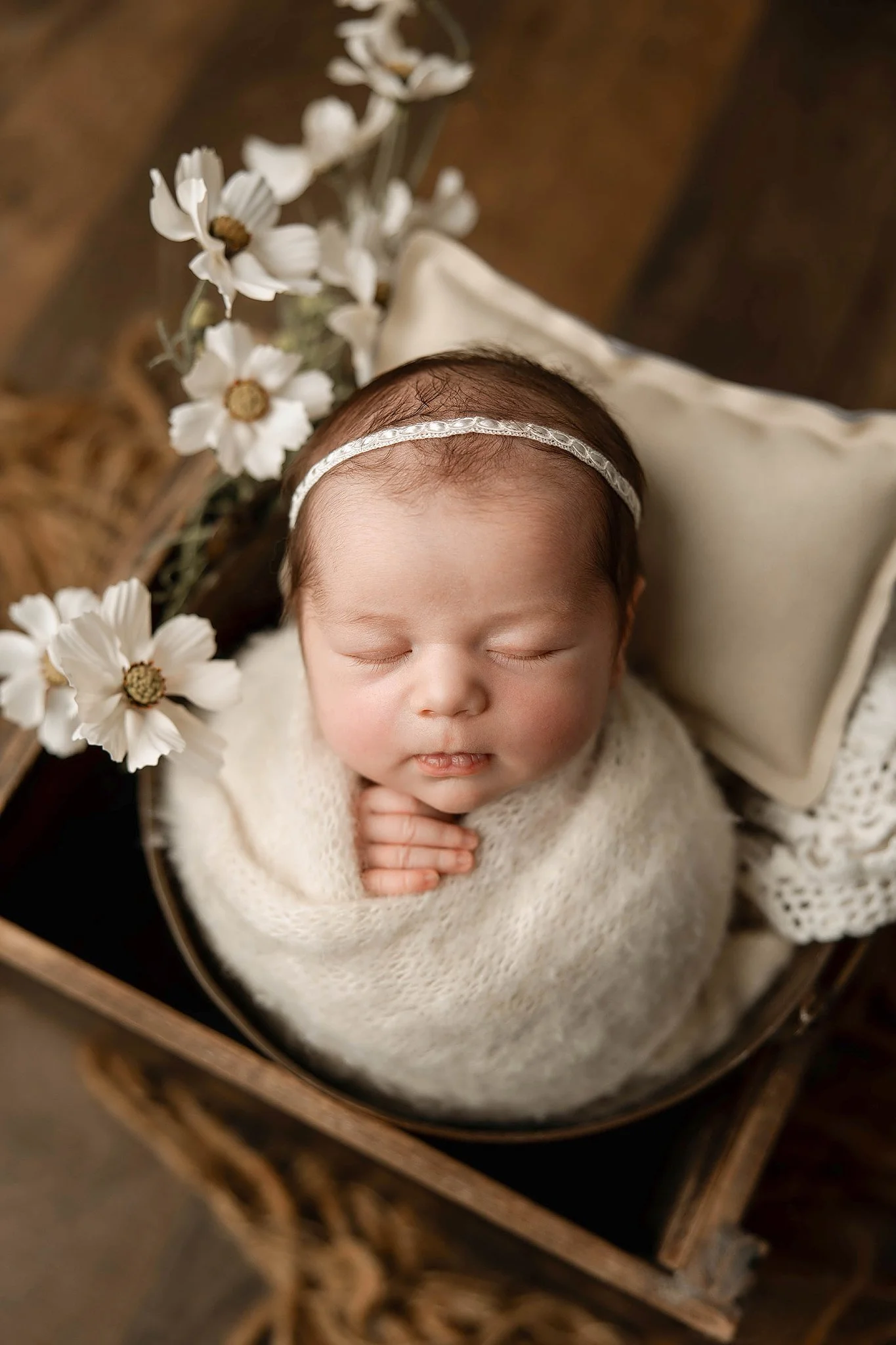 professionally posed newborn photo of a two week old baby girl wrapped up in a soft ivory knit swaddle with her hand propped out near her chin