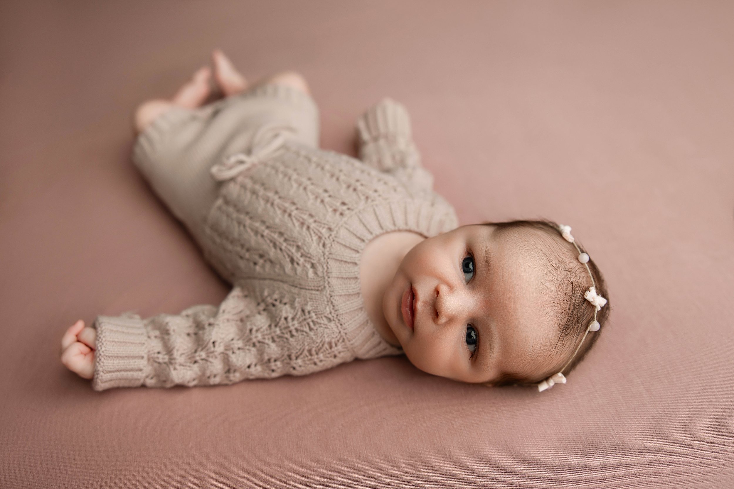 newborn baby away and posing comfortably in a mauve sweater romper
