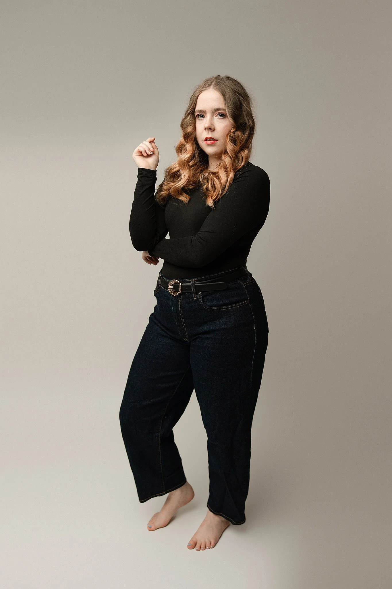 instudio senior photo with a class all white background and senior girl in jeans and a black fitted shirt